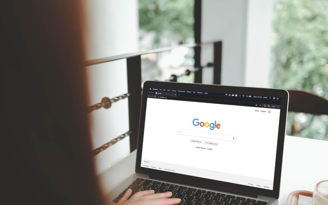 A person using a laptop with the Google homepage open on the screen in a bright room.