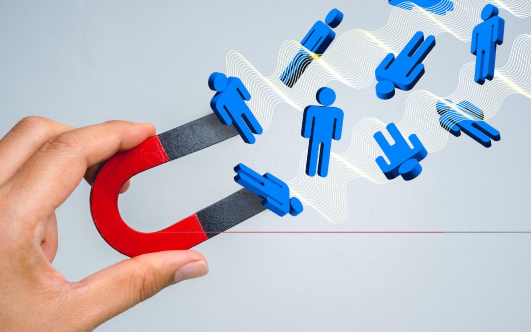 A hand holds a magnet attracting blue human icons, symbolizing attracting people or customers.