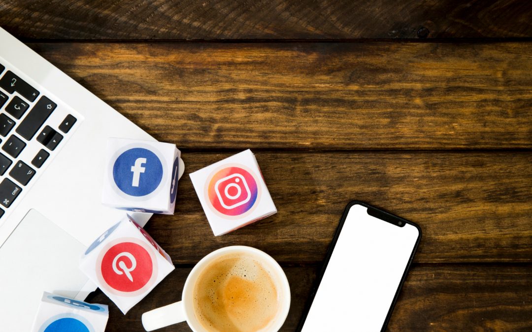 A coffee, smartphone, laptop, and cubes with social media logos on a wooden table.